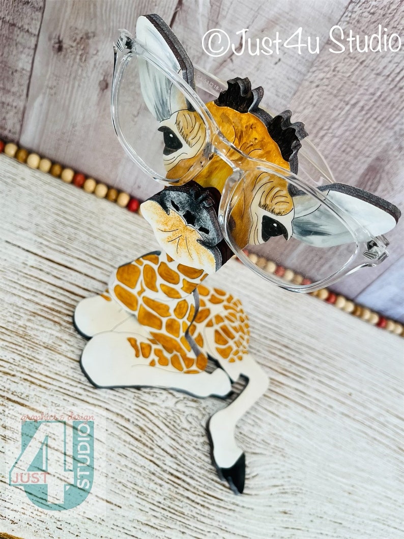 K&ouml;nnte beinhalten: Ein skurriler Brillenhalter in Form einer Giraffe. Der Halter ist mit einem Giraffenmuster in Braun- und Wei&szlig;t&ouml;nen bemalt. Klare Brillen liegen auf dem Halter. Der Text "Just4u Studio" ist sichtbar.