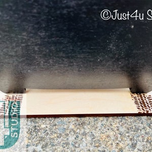 Pu&ograve; includere: Un cartello nero in ardesia con un supporto in legno. Il supporto ha un disegno a battistrada di pneumatico sul davanti e sul retro. Il cartello dice "&copy;Just4u Studio".