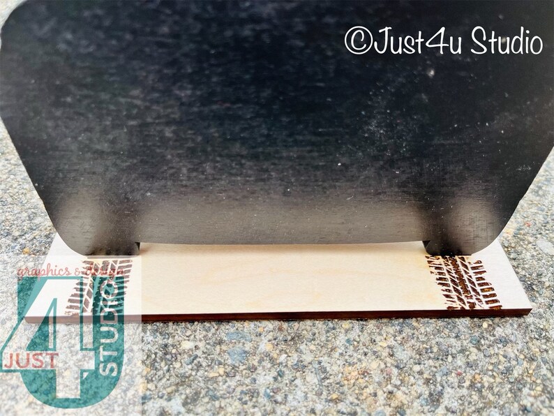 Pu&ograve; includere: Un cartello nero in ardesia con un supporto in legno. Il supporto ha un disegno a battistrada di pneumatico sul davanti e sul retro. Il cartello dice "&copy;Just4u Studio".