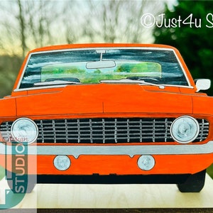 May include: A front view of a bright orange vintage car with a black grill and silver trim. The car is painted on a wooden surface.