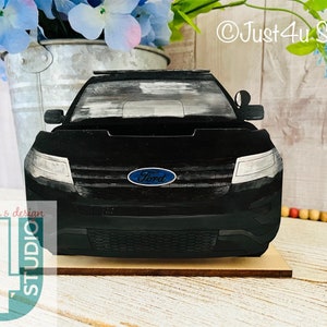 Pu&ograve; includere: Modello in legno nero di una Ford Explorer della polizia con una barra luminosa blu e bianca sul tetto. L'auto &egrave; su una base in legno. L'auto ha un logo Ford blu sul davanti.