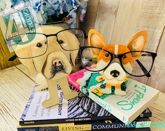 Könnte beinhalten: Zwei hölzerne Hundefiguren, die eine Brille tragen. Der Hund links ist ein gelber Labrador Retriever und der Hund rechts ist ein brauner und weißer Corgi. Die Hunde stehen auf einem Stapel Bücher.