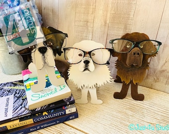 Könnte beinhalten: Drei hundeartige Metall-Buchstützen mit Brillen. Die Buchstützen sind braun, weiß und braun. Die Buchstützen halten einen Stapel Bücher. Die Bücher haben Titel wie "Showed In" und "Living into Community".