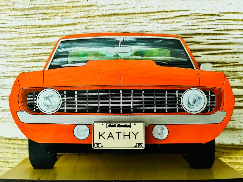 May include: A red vintage car with a black grille and chrome accents. The car has a personalized license plate that reads "Kathy".