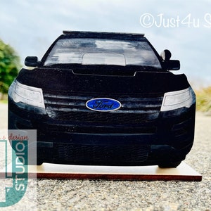 Pu&ograve; includere: Vista frontale di un SUV Ford nero con il logo Ford sulla griglia anteriore. Il veicolo &egrave; su una base di legno.