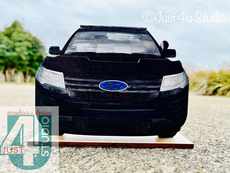 Pu&ograve; includere: Vista frontale di un SUV Ford nero con il logo Ford sulla griglia anteriore. Il veicolo &egrave; su una base di legno.