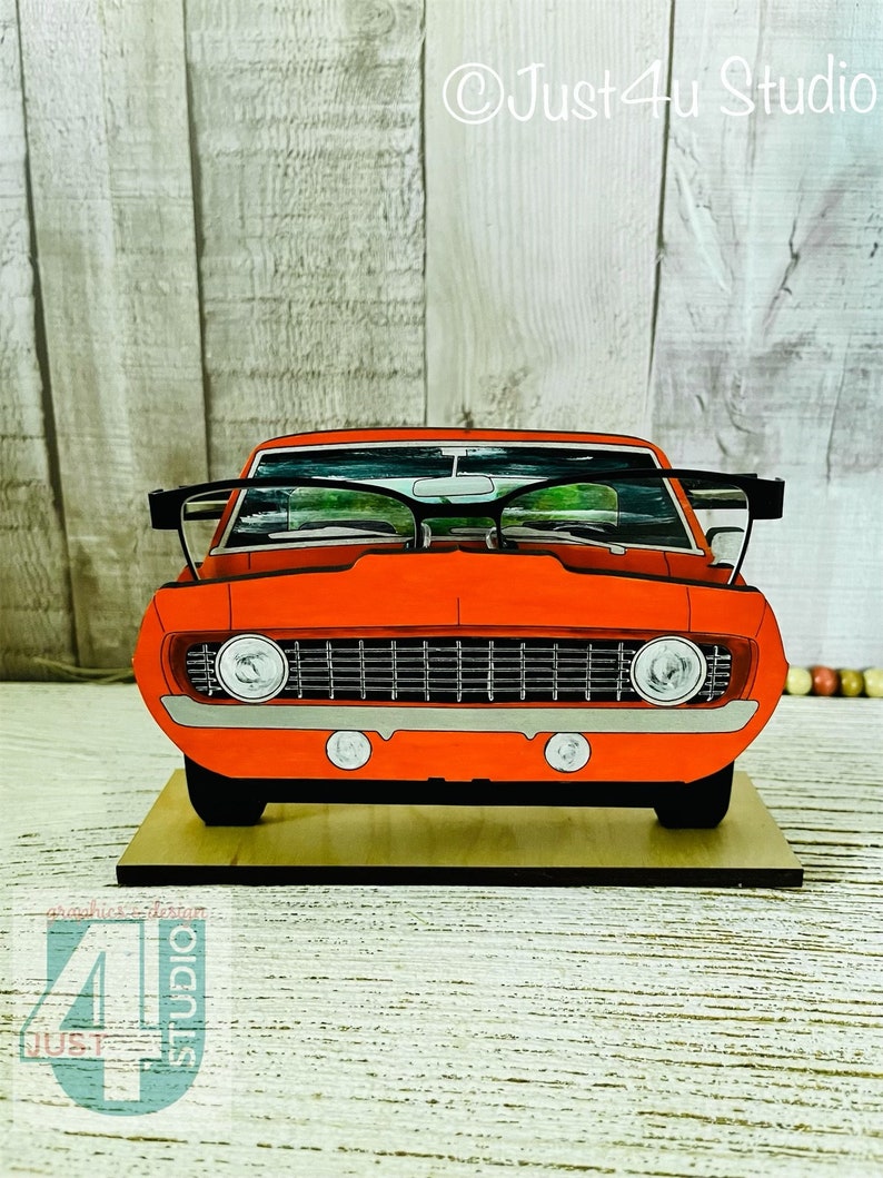 May include: A red vintage car with a black grill and headlights. The car is on a wooden base and has a pair of glasses on top of the windshield. The text "Just4u Studio" is visible in the upper right corner of the image.