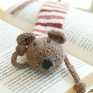 May include: A brown knitted mouse bookmark with a red and white striped tail. The bookmark is lying on a book.