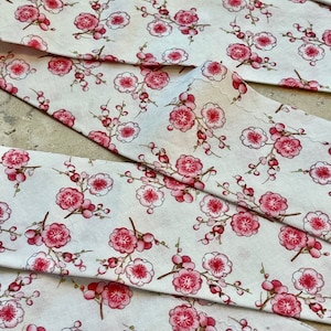 May include: White fabric with a repeating pattern of pink and white flowers. The fabric is folded in thirds, showing the pattern from different angles.