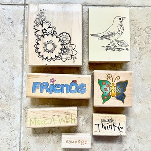 May include: A set of six wooden stamps with various designs. The stamps feature a floral design, a bird, a butterfly, the word "Friends", the phrase "Make a Wish", and the phrase "Turn on the Twinkle".