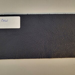 May include: A close-up of a dark blue leather swatch with the text "BLUE COW" written on a white label.