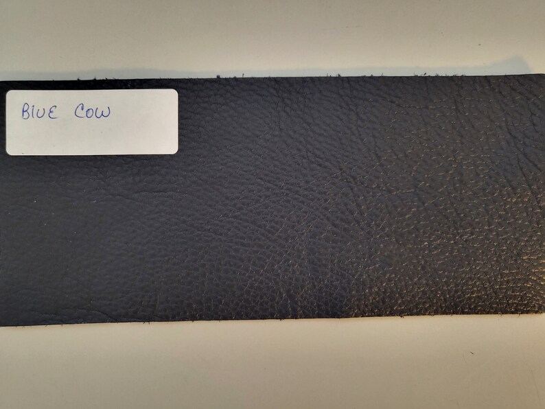 May include: A close-up of a dark blue leather swatch with the text "BLUE COW" written on a white label.