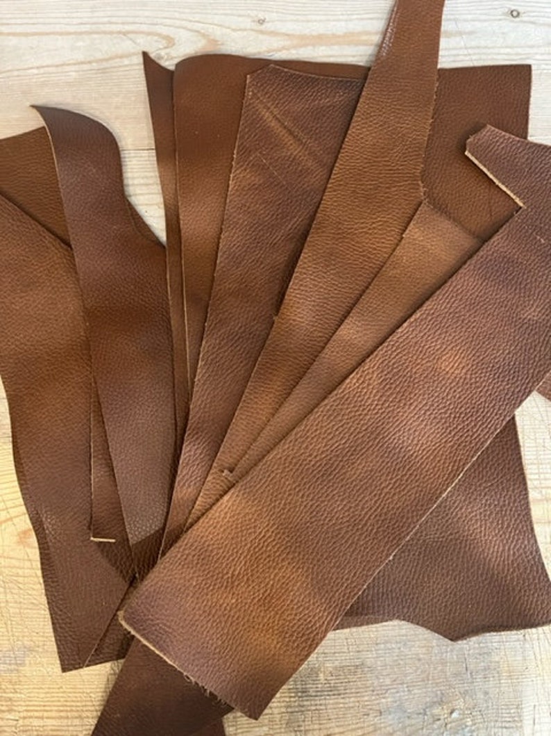 May include: A pile of brown leather scraps, some with irregular edges, ready for crafting projects.