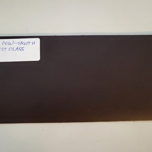 May include: A dark brown leather sheet with a white label that reads "BROWN COW - SMOOTH FIRST CLASS".