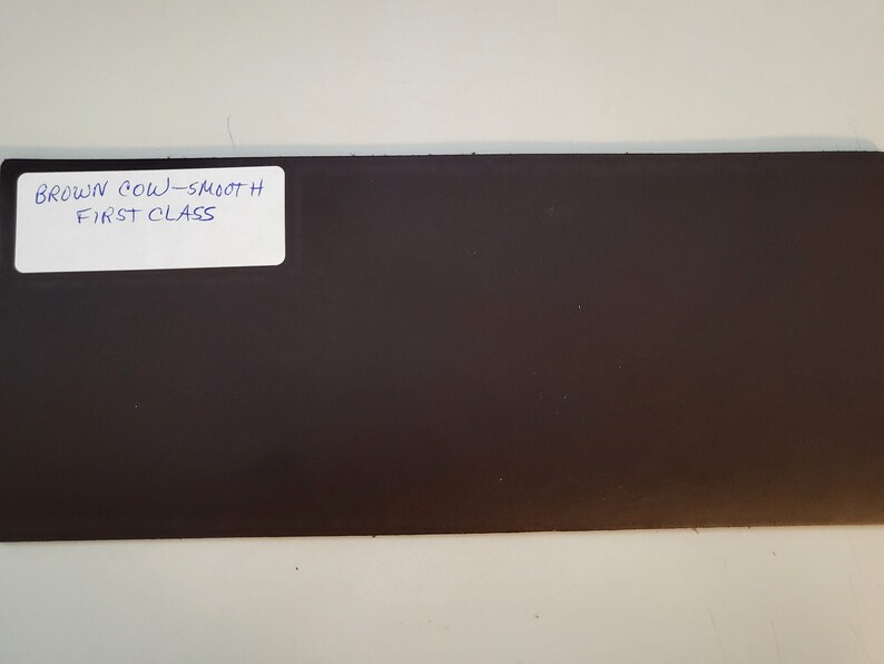 May include: A dark brown leather sheet with a white label that reads "BROWN COW - SMOOTH FIRST CLASS".