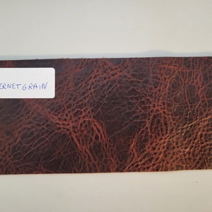 May include: A close-up of a brown leather sample with a grainy texture. The sample is labeled "COW CABERNET GRAIN".