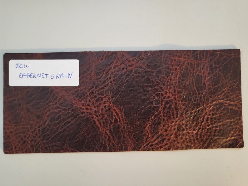 May include: A close-up of a brown leather sample with a grainy texture. The sample is labeled "COW CABERNET GRAIN".