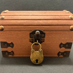 May include: A wooden treasure chest with a brass padlock and metal accents. The chest is closed and has a brown finish.