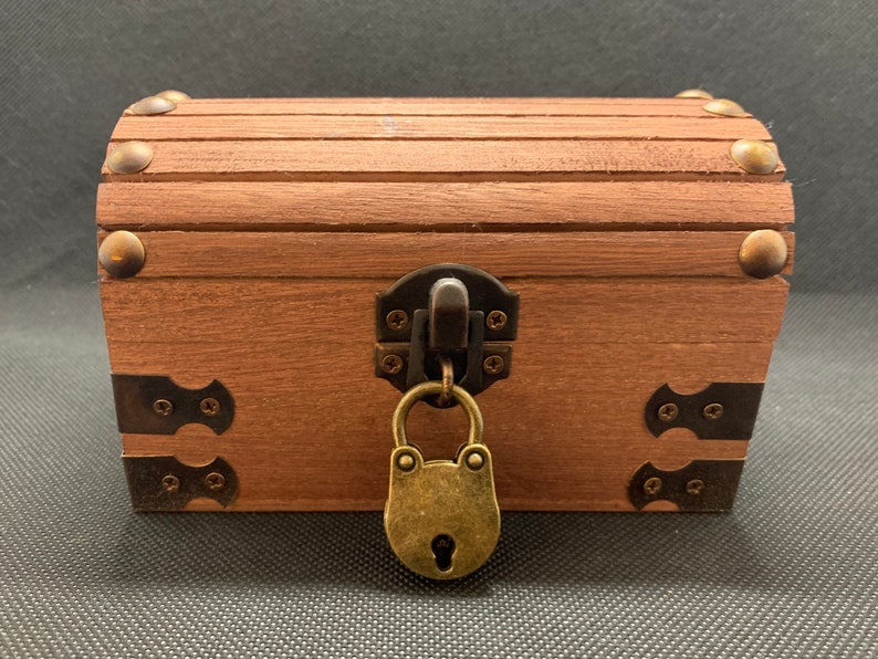 May include: A wooden treasure chest with a brass padlock and metal accents. The chest is closed and has a brown finish.