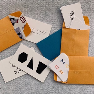 May include: A collection of cards with various designs and text, including geometric shapes, letters, and a hand sign. The cards are arranged on a brown surface with a blue background.