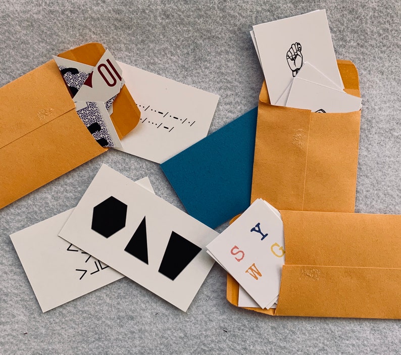 May include: A collection of cards with various designs and text, including geometric shapes, letters, and a hand sign. The cards are arranged on a brown surface with a blue background.