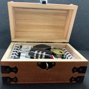 May include: A wooden treasure chest with a combination lock, a key, and a metal clasp. The chest is open and the inside is lined with white paper.