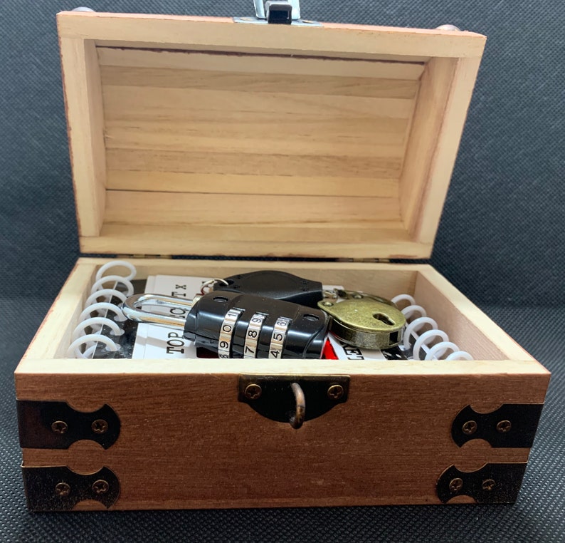 May include: A wooden treasure chest with a combination lock, a key, and a metal clasp. The chest is open and the inside is lined with white paper.