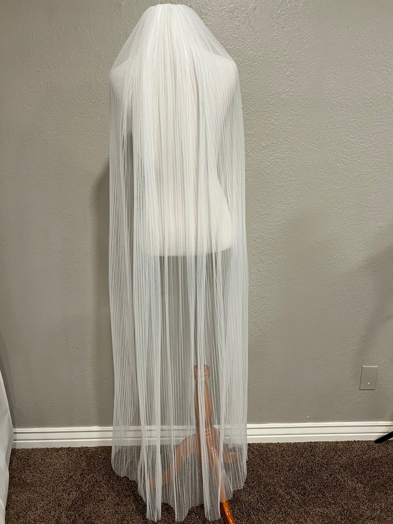 May include: A white tulle wedding veil with a pleated design. The veil is displayed on a mannequin.