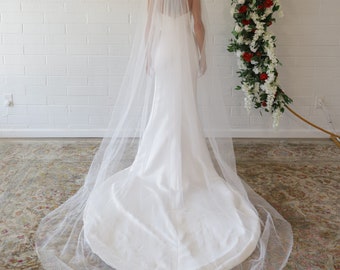 May include: A white bridal veil with a long, flowing train. The veil is made of soft tulle and has a delicate lace trim.
