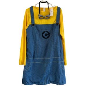 May include: A long-sleeved yellow shirt attached to a blue denim-look jumper dress featuring a black G logo on the chest pocket and white decorative stitching. The garment includes a pair of gray plastic goggles with a black strap attached at the neck.