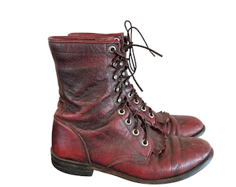 May include: A pair of dark red leather lace-up boots featuring a mid-calf height, silver-toned metal eyelets, dark brown laces, and a decorative fringed kiltie panel over the vamp. The boots have a rounded toe and a low stacked heel.