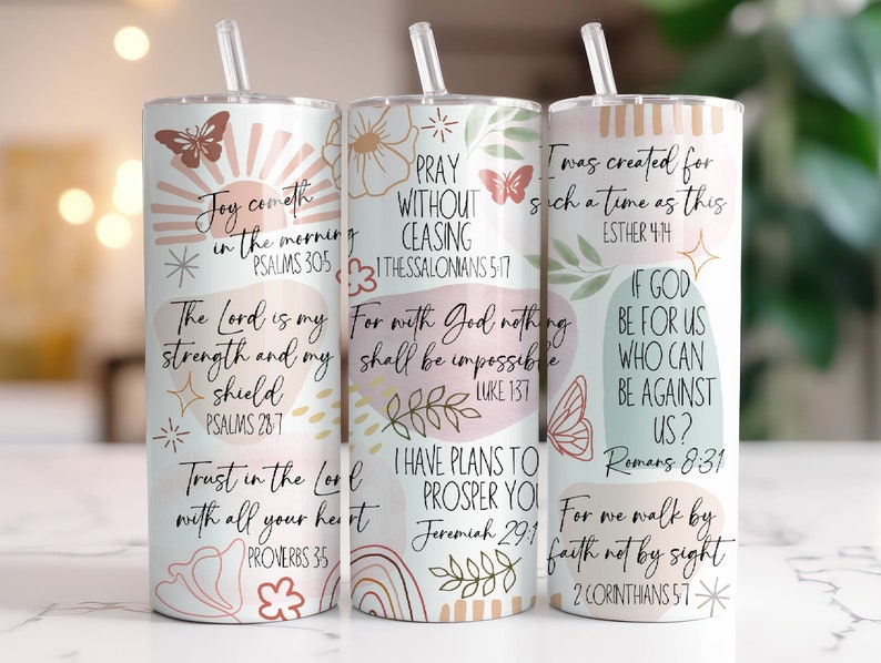 May include: Three stainless steel tumblers with inspirational bible verses and abstract floral designs. The tumblers are white with pink, peach, and green accents. The verses are: "Joy cometh in the morning", "Pray without ceasing", and "I was created for such a time as this".