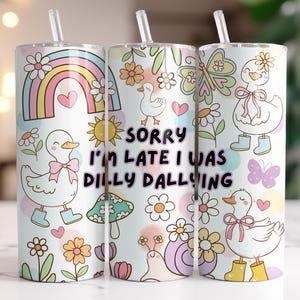 Op de afbeelding: Drie witte geïsoleerde bekers met rietjes, versierd met een grillig ontwerp. Het ontwerp omvat een regenboog, eenden, bloemen, vlinders en de tekst "SORRY I'M LATE I WAS DILLY DALLYING". De bekers zijn cilindrisch.