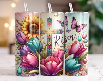 Puede incluir: Un juego de tres vasos de acero inoxidable con un diseño floral y una cruz. Los vasos presentan un patrón floral colorido con tulipanes, girasoles y mariposas. La cruz está adornada con detalles intrincados y la palabra "Risen" está escrita en el vaso.