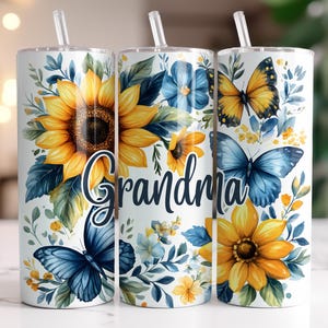 May include: Three stainless steel tumblers with a white background and floral design. The tumblers feature sunflowers, butterflies, and the word "Grandma".