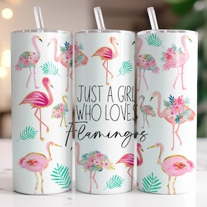 Pode incluir: Três copos de aço inoxidável com fundo branco e ilustrações de flamingos cor-de-rosa. Os copos têm uma tampa branca e um canudo transparente. O copo do meio tem o texto "Just a girl who loves flamingos".