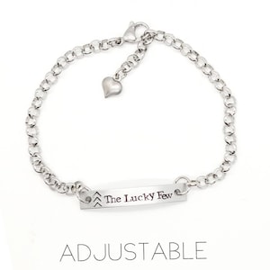 May include: Silver chain bracelet with a heart charm and a bar charm that says "The Lucky Few". The bracelet is adjustable.