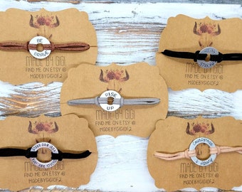 May include: Five bracelets with different inspirational messages on round metal charms. The bracelets are made with brown, gray, black, and beige cords. Each card has a floral design and the text "Made by Gigi" with instructions to find the seller on Etsy.