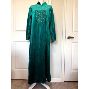 May include: A long, emerald green velvet robe with long sleeves and a high collar. The robe features a decorative embroidered design on the bodice and a full-length zipper. The robe is displayed on a white dress form.