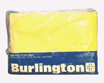May include: A yellow full fitted sheet in plastic packaging. The sheet fits a 137 x 190 cm mattress. The packaging has a blue banner with the brand name "Burlington" in white letters. The packaging also states the sheet is no-iron percale.