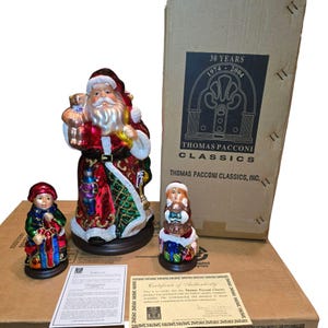 May include: A collection of Thomas Pacconi Classics Christmas figurines. The set includes a Santa Claus figure, a child figure, and a smaller figure. The figures are on a brown base and are in a box that reads "30 YEARS 1974-2004".