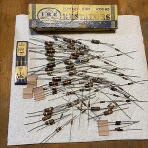 May include: A collection of vintage IRC power wire wound resistors with metal leads, accompanied by a rectangular yellow and blue box labeled Power Wire Wound Resistors and a smaller vertical box labeled 2.2 Megohms 5% Handy Pak.