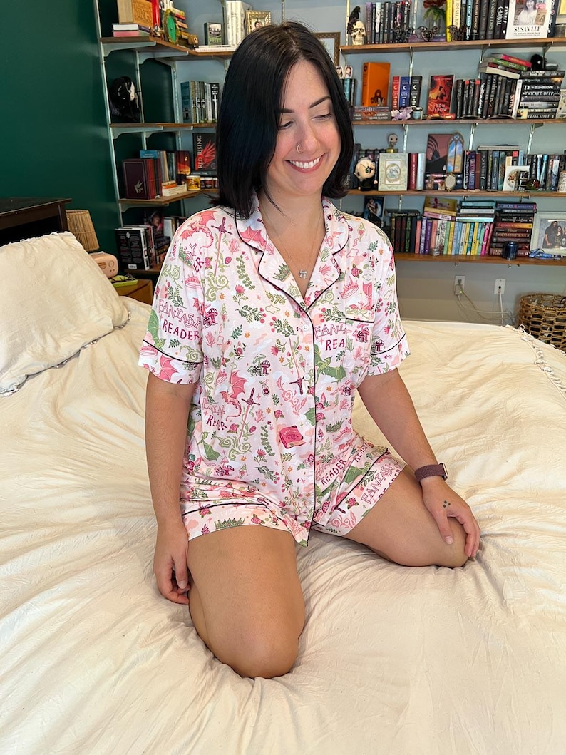 Puede incluir: Conjunto de pijama blanco con estampado de fantas&iacute;a rosa y verde. La camiseta de manga corta y los pantalones cortos presentan un patr&oacute;n repetido de dragones, flores y las palabras "Fantasy Reader". El conjunto tiene ribetes rosa oscuro.