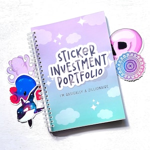 May include: A pastel blue and purple spiral bound notebook with the text "Sticker Investment Portfolio" and "I'm basically a zillionaire" on the cover. The notebook is decorated with stickers of a skull, a mandala, and an octopus.