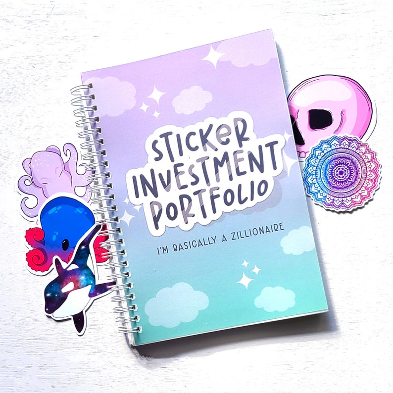 May include: A pastel blue and purple spiral bound notebook with the text "Sticker Investment Portfolio" and "I'm basically a zillionaire" on the cover. The notebook is decorated with stickers of a skull, a mandala, and an octopus.