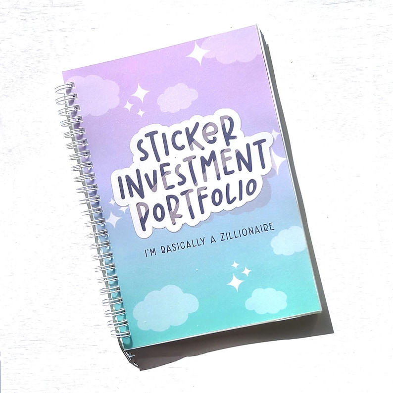 May include: A purple and blue spiral bound notebook with a sticker that says "Sticker Investment Portfolio" and the text "I'm basically a zillionaire". The notebook has a cloud and star design.