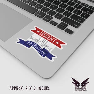 A vinyl sticker with a patriotic design. A red banner at the top reads "Dissent" between two stars; gray text in the middle reads "is the highest form of;" and a blue banner at the bottom reads, "Patriotism." Shown on a MacBook.