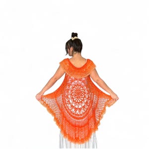 May include: An orange crochet shawl with a circular design and scalloped edges. The shawl is sleeveless and has a rounded neckline. The intricate openwork pattern is visible throughout the garment, creating a delicate and airy appearance.