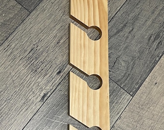 May include: A wooden wine glass holder with four circular cutouts and angled slots. The holder is made of light-colored wood and features a green alligator graphic at the bottom. The design is for wall mounting.