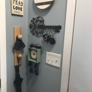 May include: A light blue wall with a wooden sign that says "Eat Pray Love" and a round wooden sign with the words "New Orleans" and a skyline silhouette. There is a black metal key holder with keys hanging from it. There is a wooden hook with a black and white polka dot umbrella hanging from it. There is a small square box with a white flower inside and sunglasses hanging from it. There are three light switches on the wall.